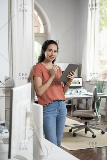 Female professional using digital tablet while standing at office doorway
