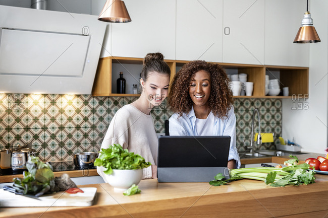 Happy female coworkers watching recipe on tablet at workplace kitchen