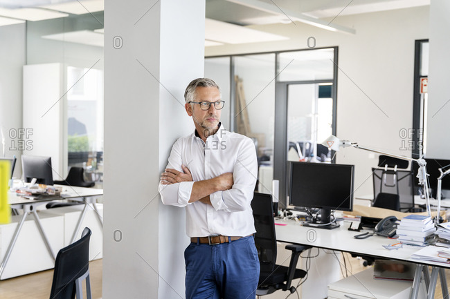 Confident businessman with arms crossed leaning on column in office