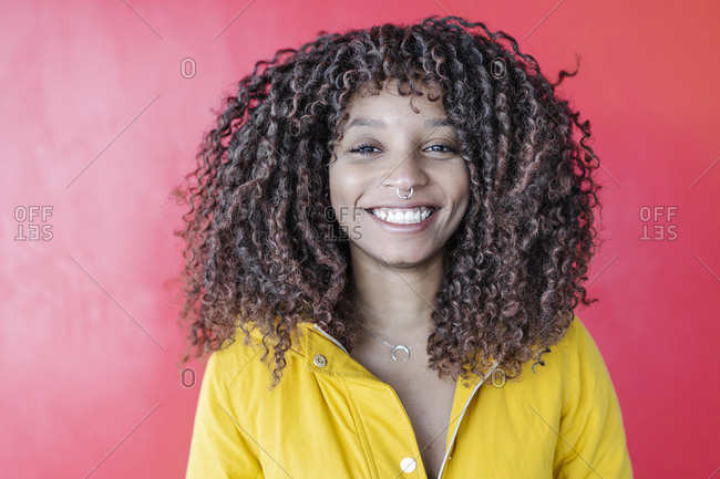 Smiling curly hair woman smiling while standing against pink wall