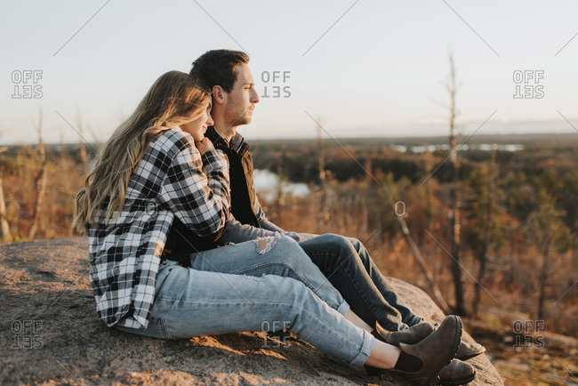 Young couple sitting together on rocky surface during autumn hike