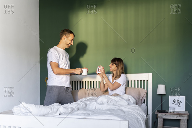 Boyfriend bringing coffee to girlfriend sitting in bed at home