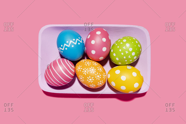 Handmade painted Easter eggs in purple tray on pink background