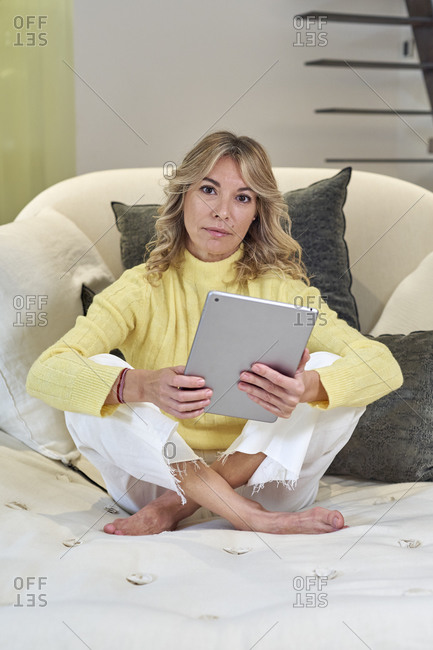 Mature woman in yellow sweater holding digital tablet at home