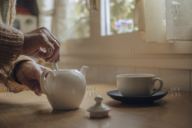 Senior woman's hands preparing tea in kettle on kitchen table
