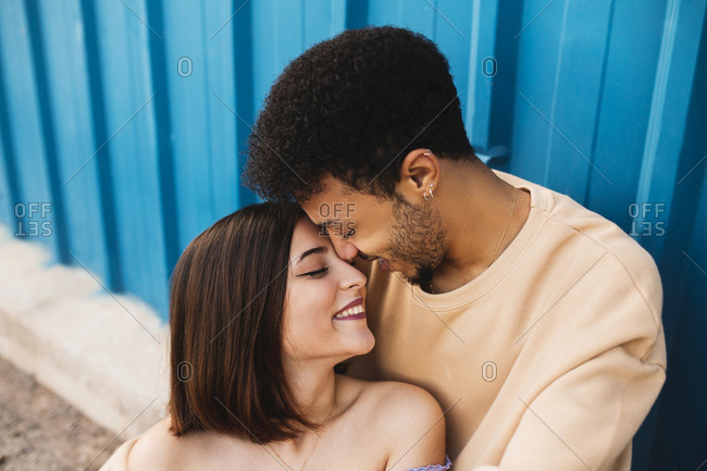 Smiling young couple sitting face to face against blue wall