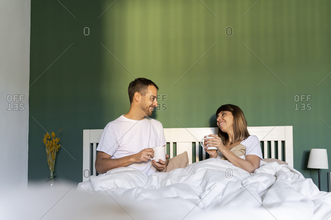 Smiling couple having coffee while sitting on bed at home