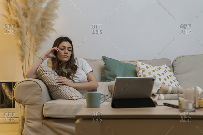 Young woman with digital tablet relaxing on sofa at home