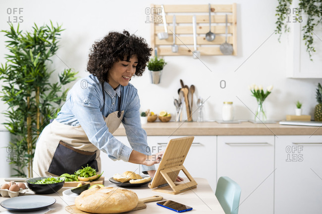 Young woman using digital tablet while preparing vegan sandwiches in kitchen