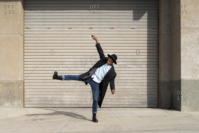 Fashionable young man standing on one leg while dancing against shutter