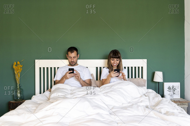 Couple using their mobile phones while sitting in bed at home
