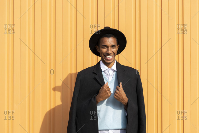 Cheerful young man holding blazer against yellow corrugated iron on sunny day