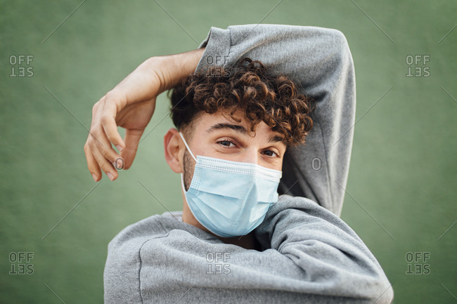 Man with hand raised wearing surgical mask against green background in studio