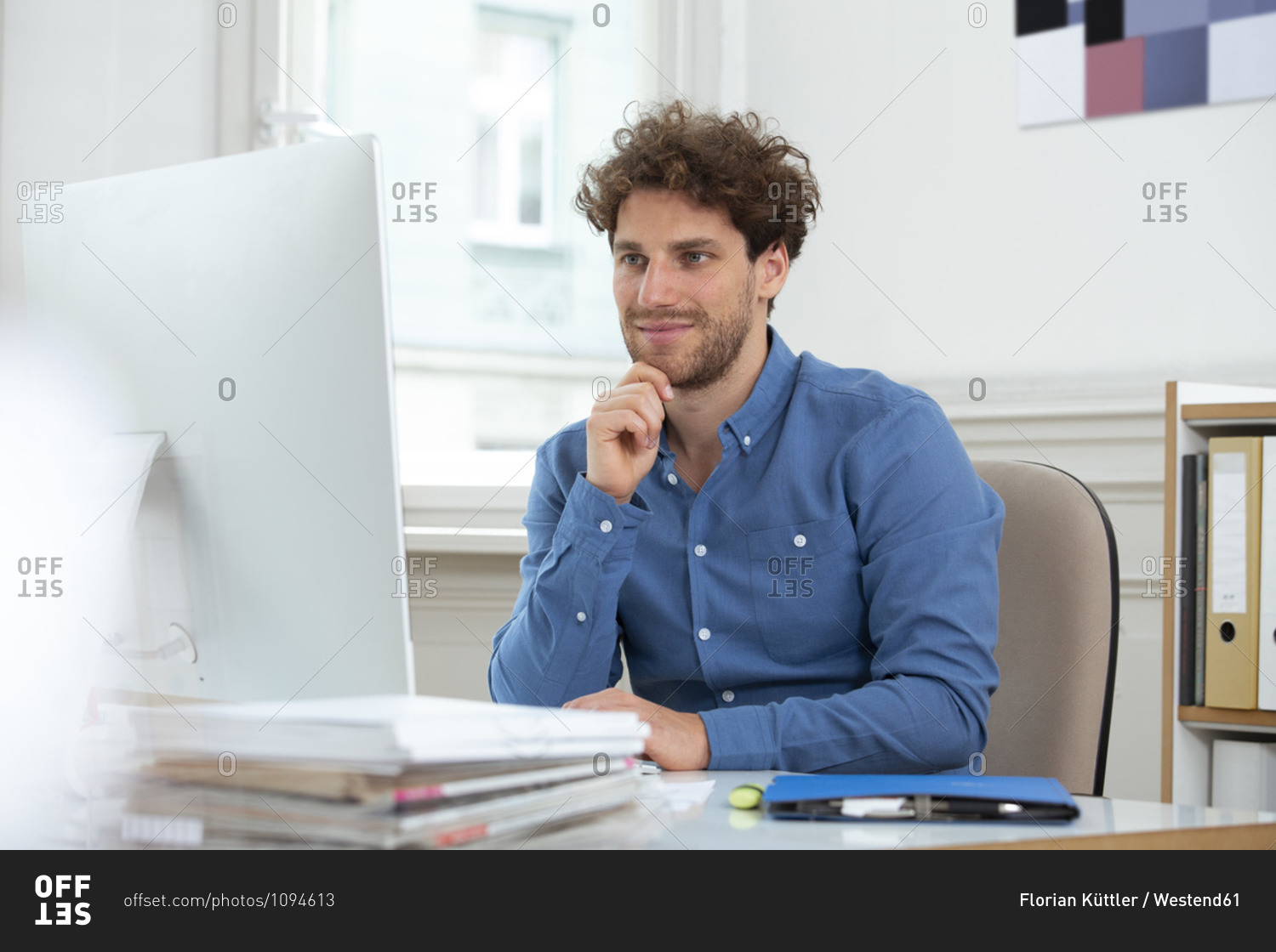 Male professional with hand on chin working over computer in office cabin