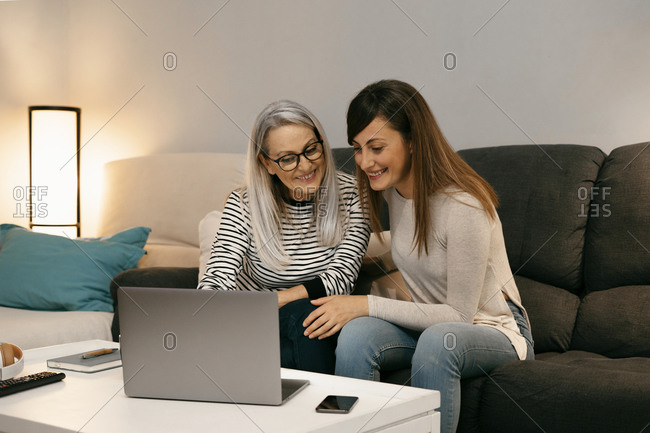 Smiling mother and daughter using laptop while sitting on sofa at home