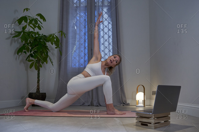 Female instructor with hand raised doing yoga in exercise room at home
