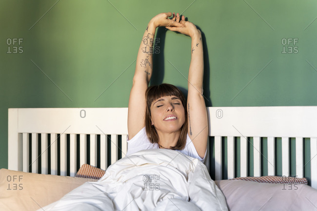 Mid adult woman stretching arms while waking up on bed at home