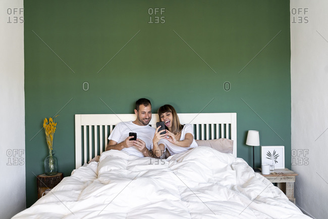Happy woman showing mobile phone to man sitting on bed at home