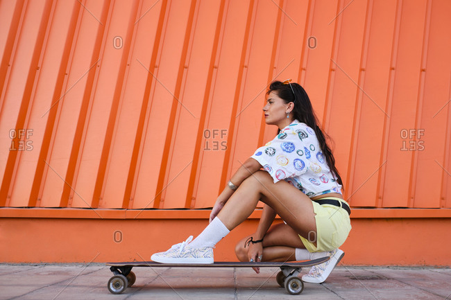 Portrait of beautiful girl crouching beside longboard in front of corrugated iron wall