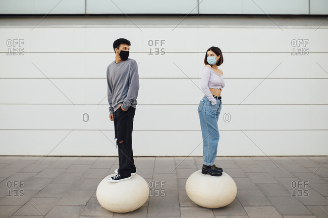 Couple with face mask looking over shoulder while standing on white concrete ball