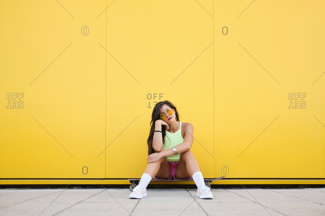 Portrait of beautiful girl sitting alone on longboard in front of yellow wall