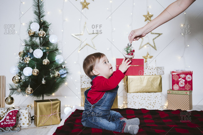 Mother giving bauble to baby boy sitting on blanket at home during Christmas
