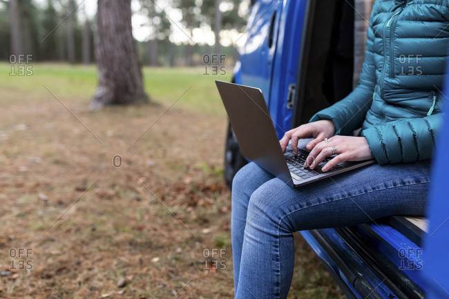 Mid adult woman using laptop in door of camper van at Cannock Chase