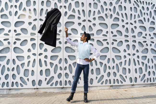 Young man standing on one leg while throwing jacket in air against pattern wall