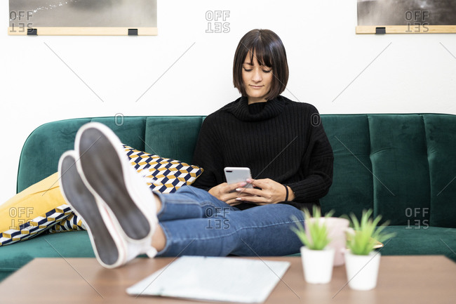 Young woman using mobile phone wile leaning legs on coffee table in living room