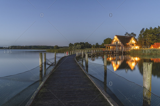Germany- Schleswig-Holstein- Hemmelsdorf- Empty pier on shore of Hemmelsdorfer See lake at dawn with house in background