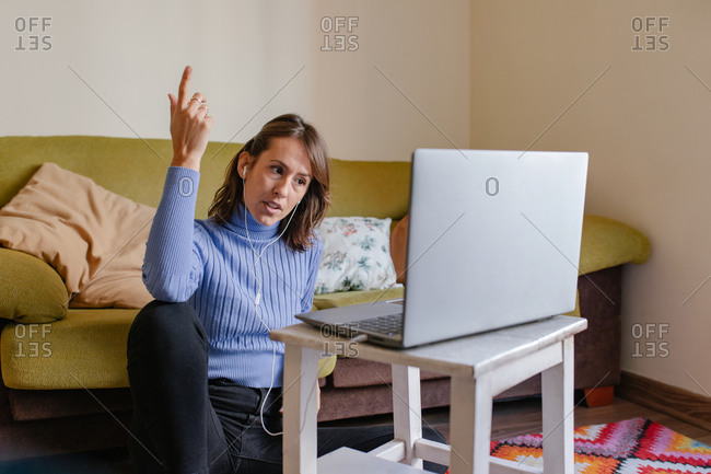 Adult female remote specialist in casual outfit discussing business issues during video conference via laptop while working in living room at home