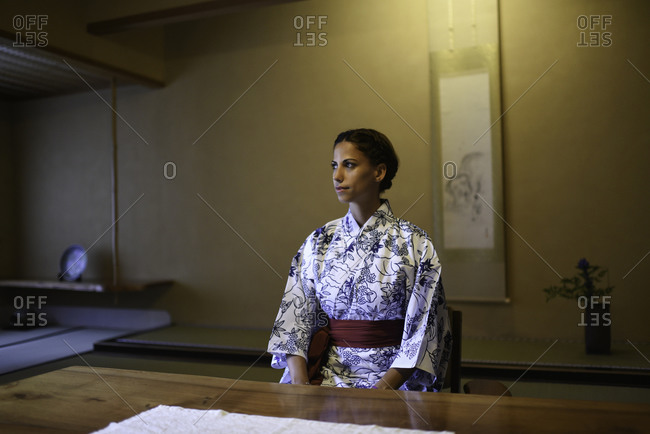 Young caucasian woman in Japanese clothes sitting at the table in ryokan room and practicing mindfulness meditation
