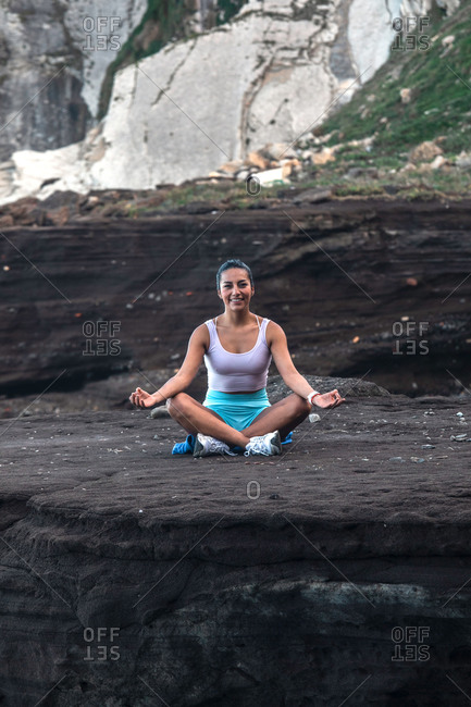 Peaceful female sitting in Lotus pose with mudra hands and meditating while doing yoga and practicing mindfulness on beach near sea