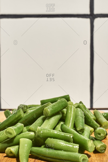 Pile of chopped green beans on wooden cutting board placed on table near glass of water in kitchen