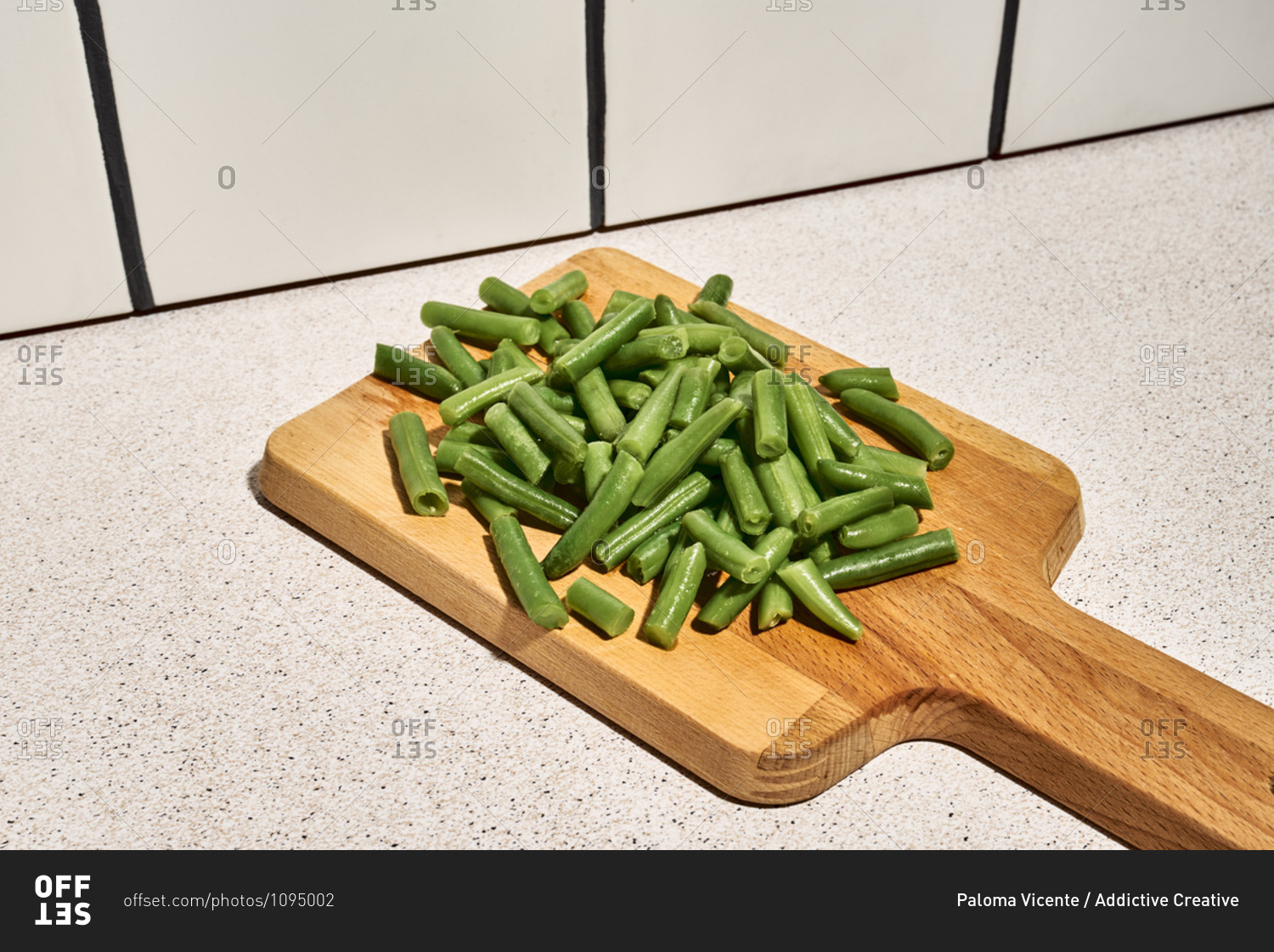 Pile of chopped green beans on wooden cutting board placed on table near glass of water in kitchen