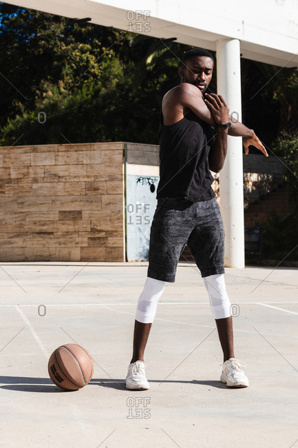 Fit African American male basketball player warming up stretching while preparing for training on sports ground in summer with eyes closed