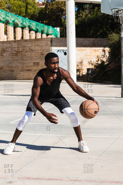 Determined African American male athlete playing basketball on court in summer