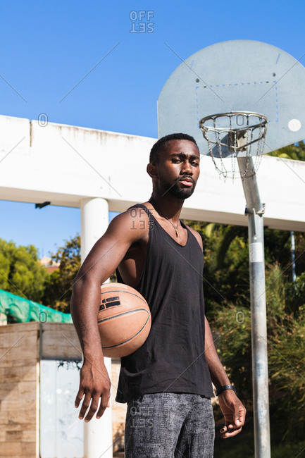 Fit African American male standing on basketball court with ball and looking at camera