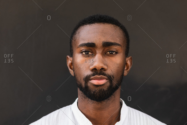 Confident African American male wearing white t shirt standing on street while looking at camera