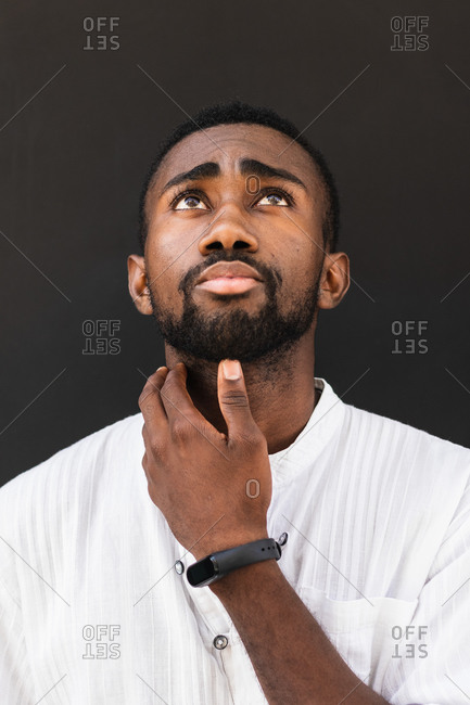 Confident African American male wearing white t shirt standing on street while looking up