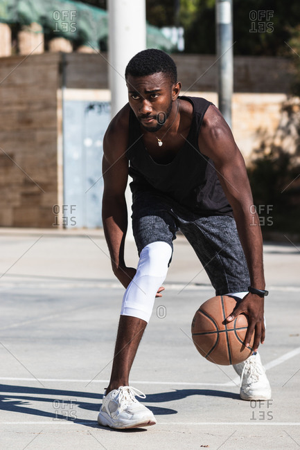 Determined African American male athlete playing basketball on court in summer