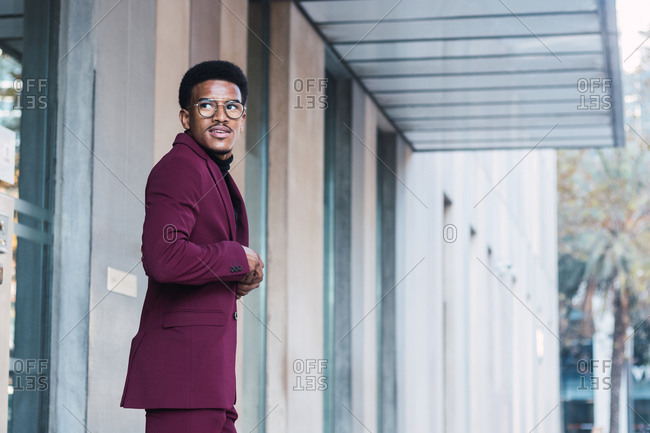 Cheerful young African American businessman in stylish suit and eyeglasses walking in street