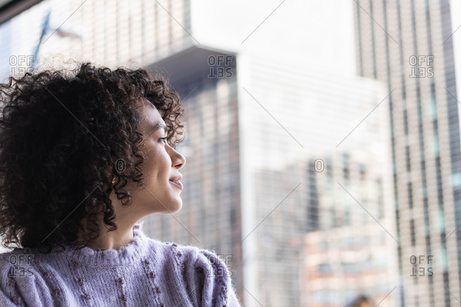Thoughtful African American female with curly hair standing with crossed arms near glass building and looking away