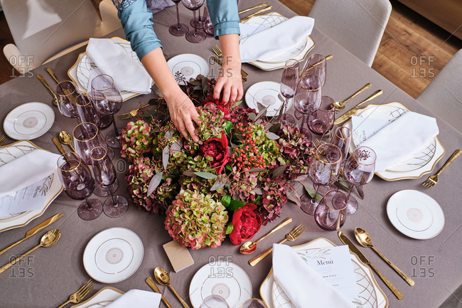 From above cropped unrecognizable female housewife setting table with delicate flowers for festive event at home