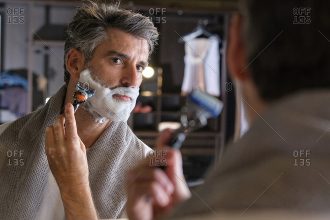 Stock photo of middle aged man with grey hair using shaving cream to shave his beard.