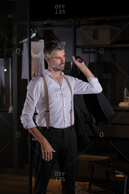 Stock photo of elegant middle aged man wearing suit and suspenders smiling and looking to the side.