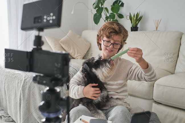 Happy boy feeding his lovely dog and filming a video for his channel.