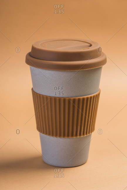 Minimalist white paper cup of takeaway coffee with brown silicone ring and lid against beige background