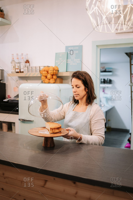 Friendly smiling female owner of confectionery cafe standing at counter and demonstrating delicious cake