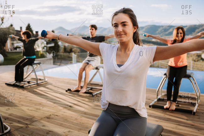 Content people sitting on pilates chairs and practicing with dumbbells while smiling and looking away